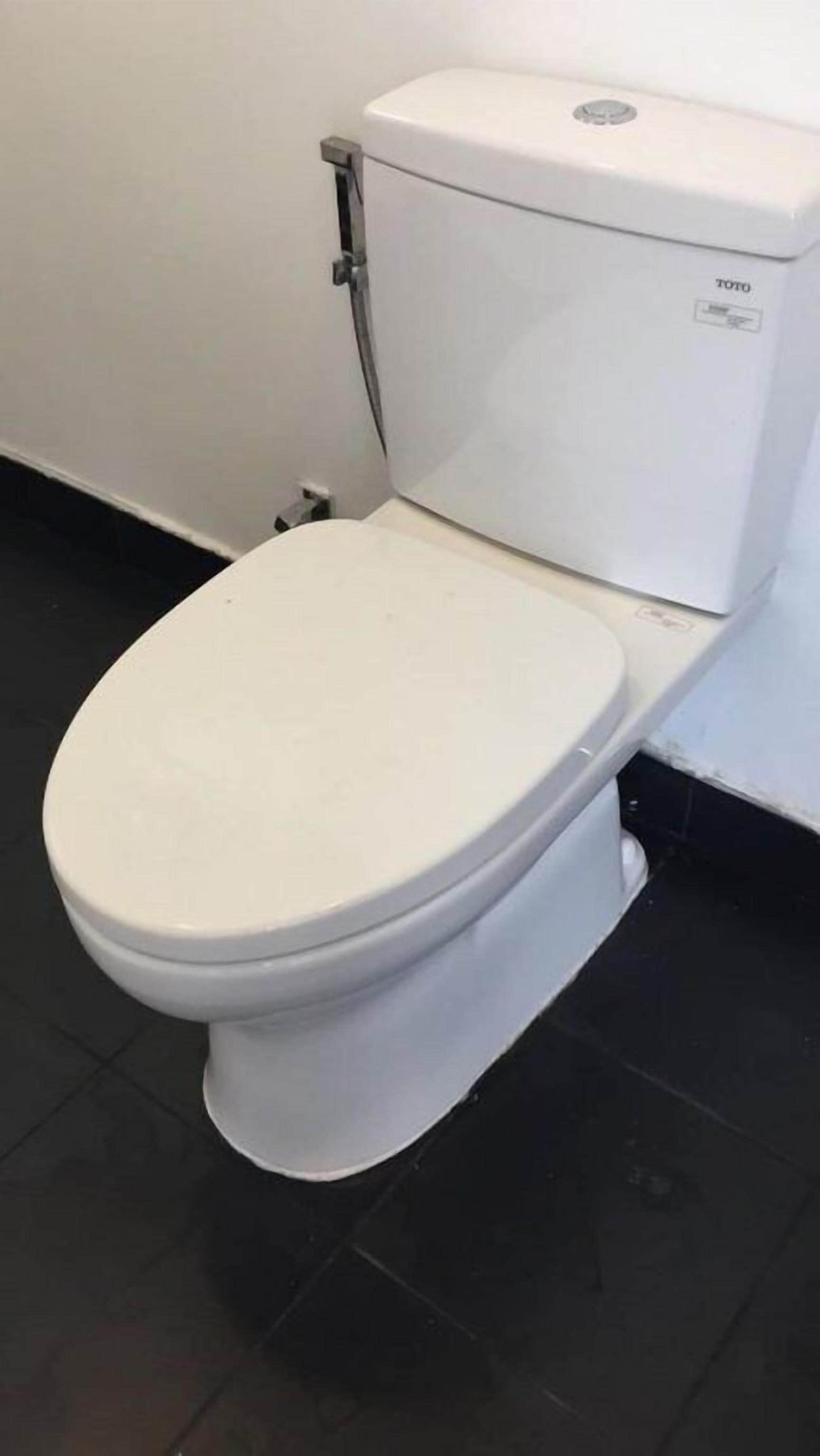 Uma sanita branca com etiqueta da marca Toto, colocada contra uma parede branca com soalho em mosaico preto.