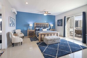 Une chambre à coucher comprenant un lit, une chaise, une table de chevet, un ventilateur de plafond et une vue sur l’extérieur.