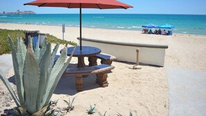 A beachside patio with a red umbrella, a round table, and a chair. - Modern Luxury Beachside Retreat (Puerto Peñasco)