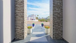 A corridor with stone walls and potted plants, leading to a building with a clear sky view. - Modern Luxury Beachside Retreat (Puerto Peñasco)