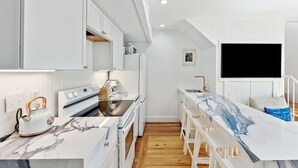 A modern kitchen with white cabinetry, a marble countertop, and a built-in oven. - Home With Private Pool 'The Blue Lagoon' (Charleston)