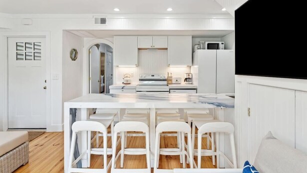 A modern kitchen with white cabinetry, a marble countertop, and a central island with bar stools. - Home With Private Pool 'The Blue Lagoon' (Charleston)