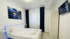 A modern hotel room with a white bed, a flat-screen TV, and a large window with curtains. - Alezzi Yaht Apartment With Sea View Near The Beach (MAMAIA SAT)