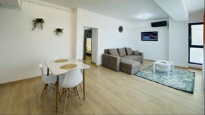 A modern living room with a dining area, a sofa, a coffee table, and a TV mounted on the wall. - Alezzi Yaht Apartment With Sea View Near The Beach (MAMAIA SAT)