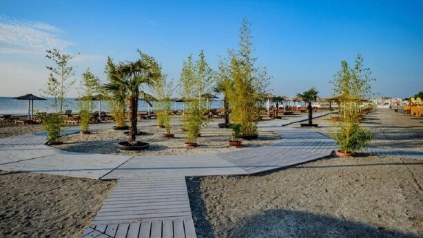 A beachside walkway with potted plants and umbrellas, leading to beach chairs and a pool area. - Alezzi Yaht Apartment With Sea View Near The Beach (MAMAIA SAT)