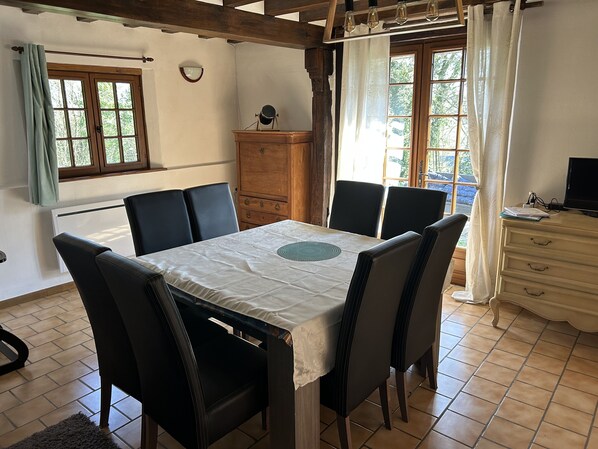 A dining area with a table set for four, surrounded by chairs, a wooden cabinet, and a television on a dresser.