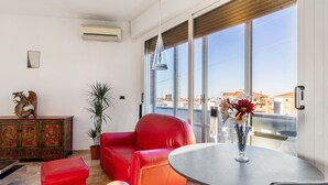 A modern living room with a red leather sofa, a small round table with a vase of flowers, and a view of the city through large windows. - 051 Living apartment within walking distance of downtown and FS station (Bologna)