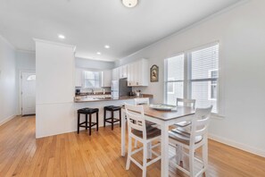 A modern kitchen with white cabinets, a wooden dining table, and bar stools. - Saagara Thira (Carolina Beach)