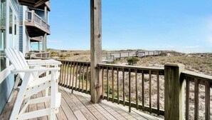 A wooden deck with a railing, overlooking a beach with a wooden boardwalk.