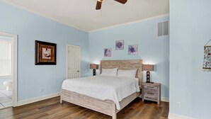 Un dormitorio con cama de madera, mesitas de noche, ventilador de techo y decoración en la pared.