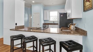 A kitchen with a granite countertop, white cabinets, a black refrigerator, and three black bar stools.