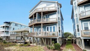 Una propiedad frente a la playa con edificios de varios pisos, balcones de madera y un paisaje arenoso.
