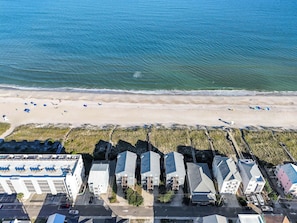 An aerial view of a coastal area with a beach, a row of residential buildings, and a parking lot. - Saagara Thira (Carolina Beach)