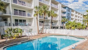 A swimming pool with a tiled deck, surrounded by a white fence and palm trees. - Oceanfront Serene 2-bedroom 2 bath in Indian Shores Florida. (Indian Shores)