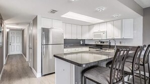 A modern kitchen with white cabinets, stainless steel appliances, and a central island with bar stools. - Oceanfront Serene 2-bedroom 2 bath in Indian Shores Florida. (Indian Shores)