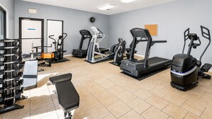 Ein Fitnessstudio mit verschiedenen Trainingsgeräten, darunter Laufbänder, Crosstrainer und Kurzhanteln.