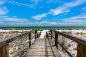 A wooden boardwalk leading to a beach with umbrellas and people.