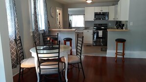 A dining area with a round table and chairs, a kitchen with white cabinets and stainless steel appliances, and a patterned wall. - Cozy Private Home @ Blue Moon Cottage in Historic Deland, Fl. (DeLand)