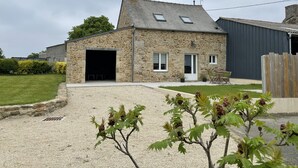 A stone house with a garage, a small patio, and a gravel driveway. - Maison 2 Proche de la mer (Saint-Lormel)