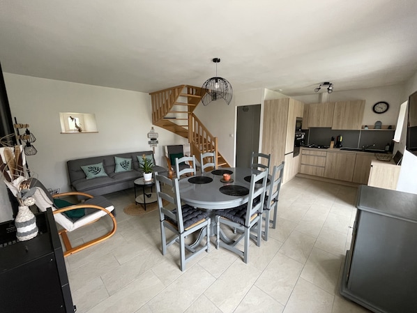 Une cuisine moderne avec des meubles en bois, un coin repas avec une table ronde et des chaises, un canapé gris avec des coussins et un escalier menant à un autre niveau.