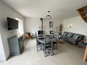 Un salon moderne comprenant un coin repas, un canapé gris et un téléviseur à écran plat fixé au mur.