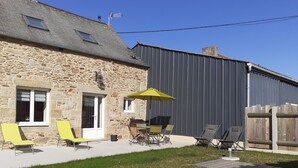 A stone building with a patio area featuring outdoor furniture and a yellow umbrella. - Maison 2 Proche de la mer (Saint-Lormel)