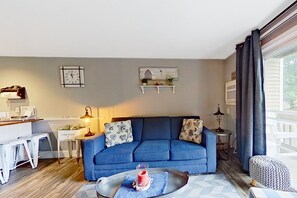Una sala de estar con un sofá azul, una mesita con una vela y una ventana con cortinas.