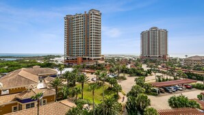 Un hotel de gran altura con varios pisos, un patio central con palmeras y vista a la playa.