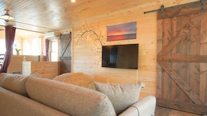 A cozy living room with a sofa, a television mounted on the wall, and a wooden barn door. - LoZa House rooftop SkyDeck lakefront  Pets Hot Tub (Plattsburgh)