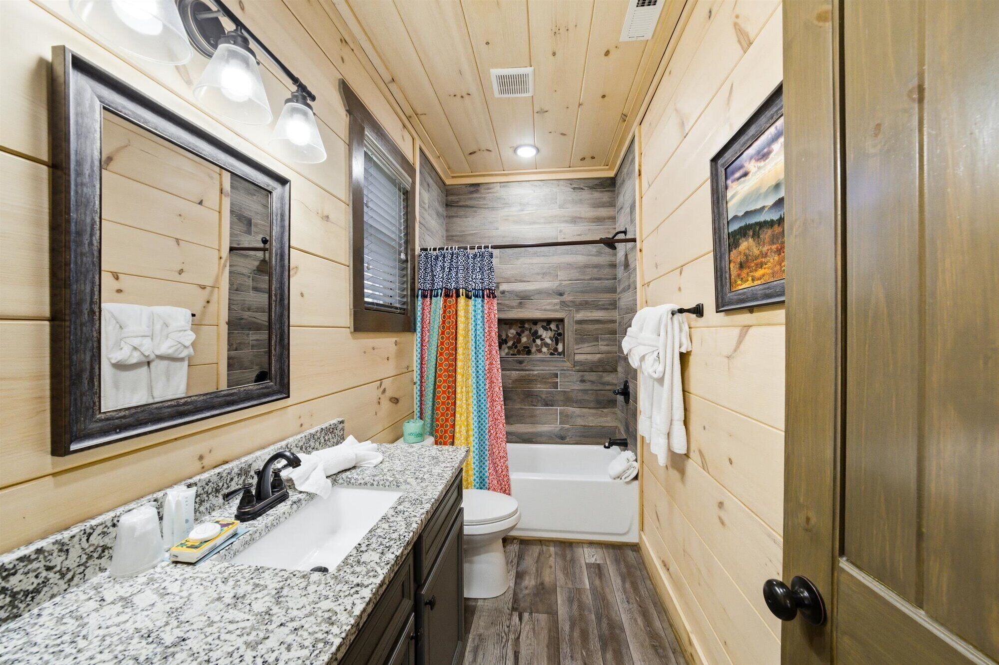 A wooden-paneled bathroom with a sink, mirror, toilet, and bathtub.