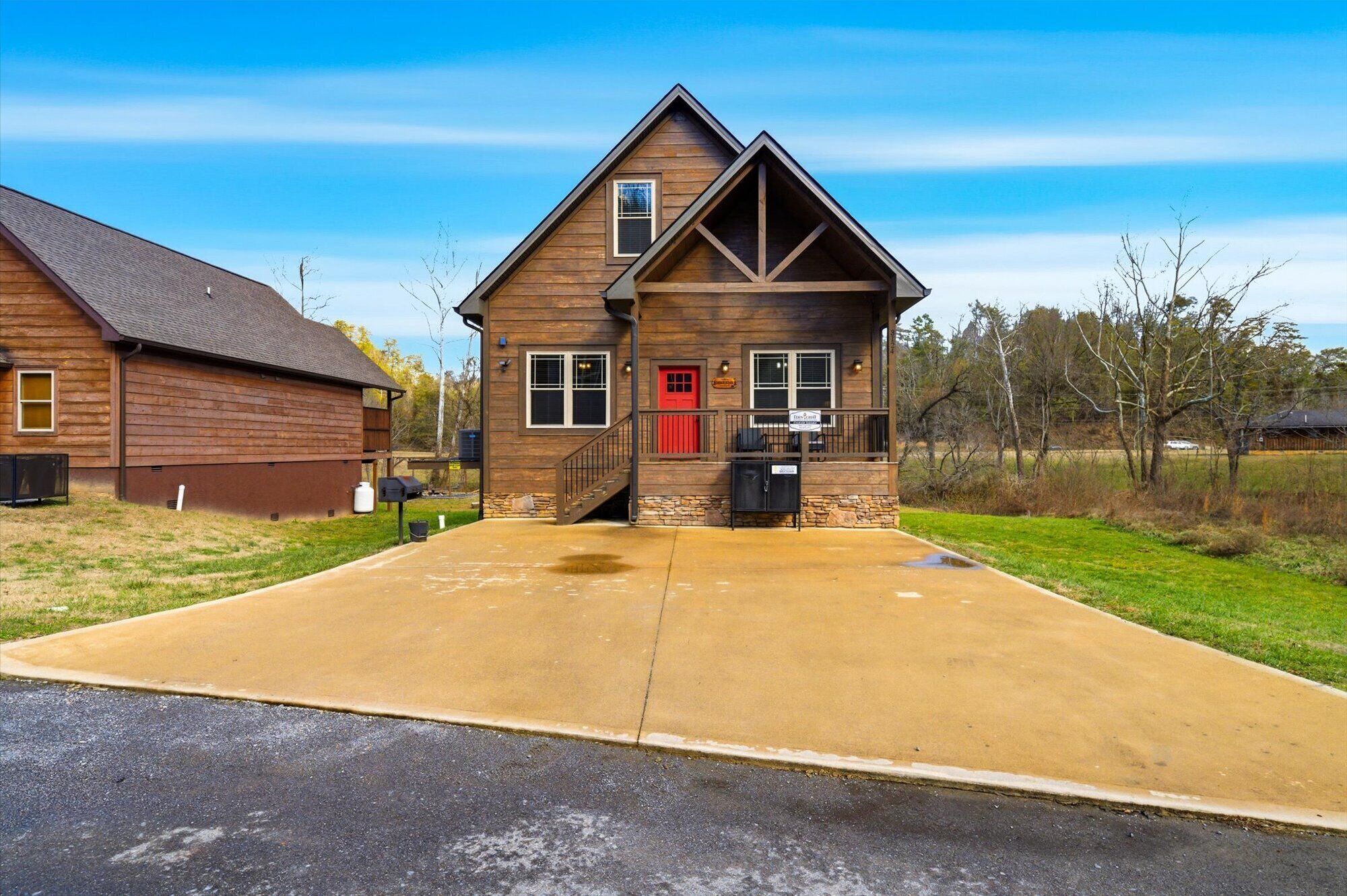 A two-story wooden house with a red door, a covered front porch, and a driveway leading to the entrance.