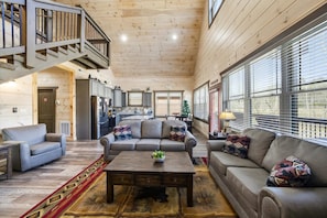 A spacious living area with a wooden ceiling, a staircase, a kitchen, and large windows. - Creekside Splendor (Sevierville)