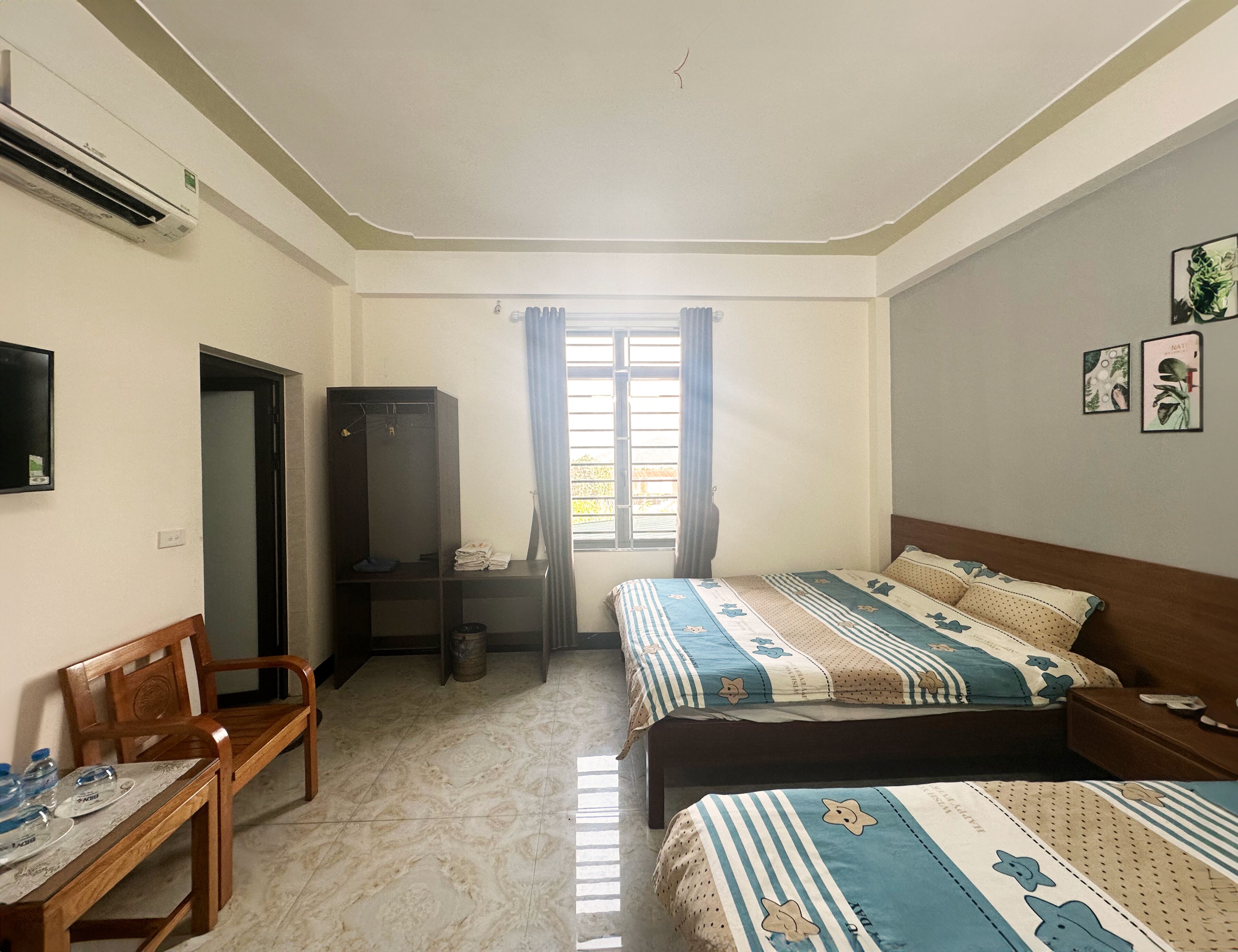 Habitación de hotel con dos camas, un escritorio con sillas, un armario y una ventana con cortinas.