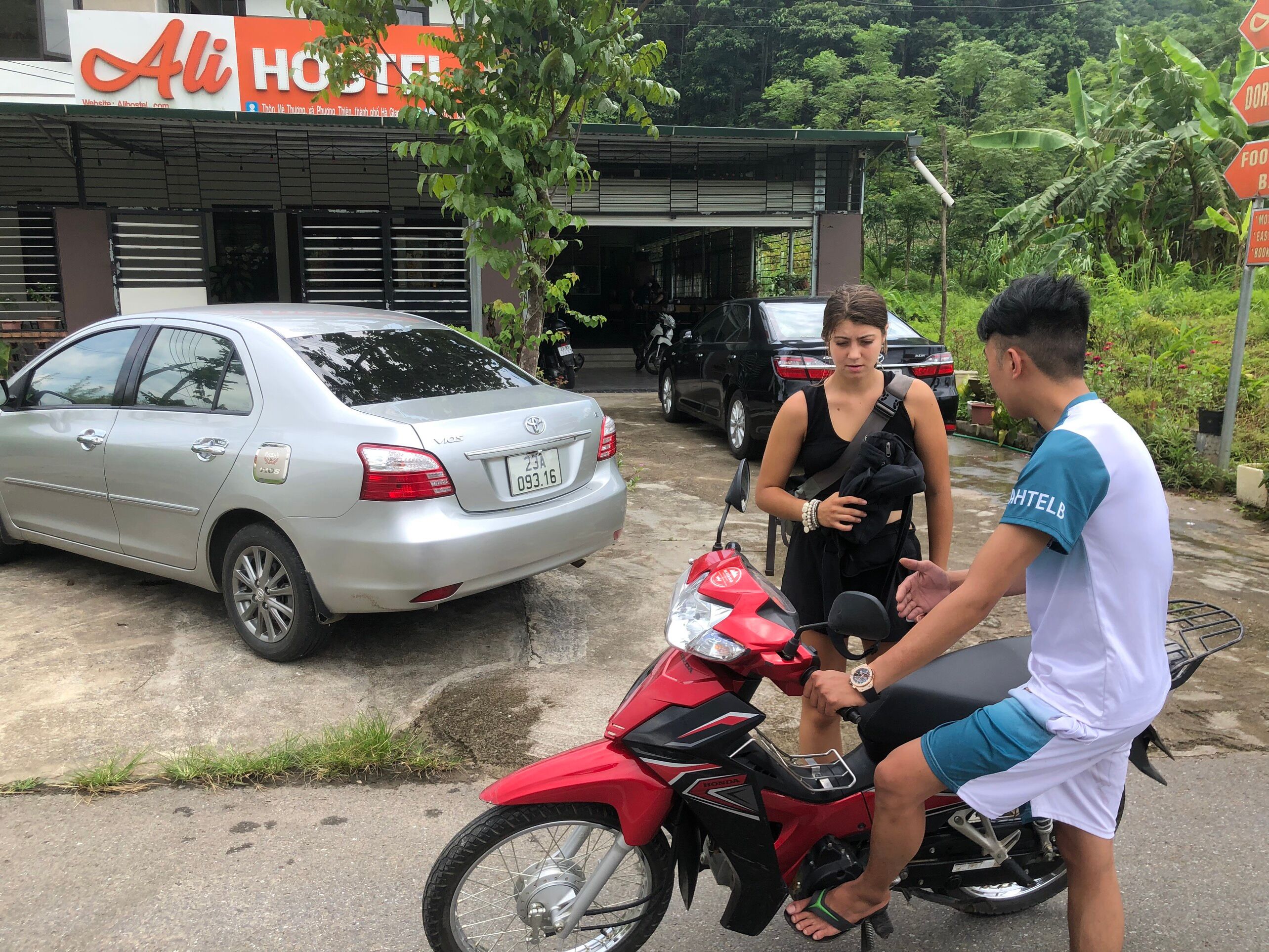 Un coche plateado estacionado frente a un edificio con un letrero que dice "Ali Hostel".