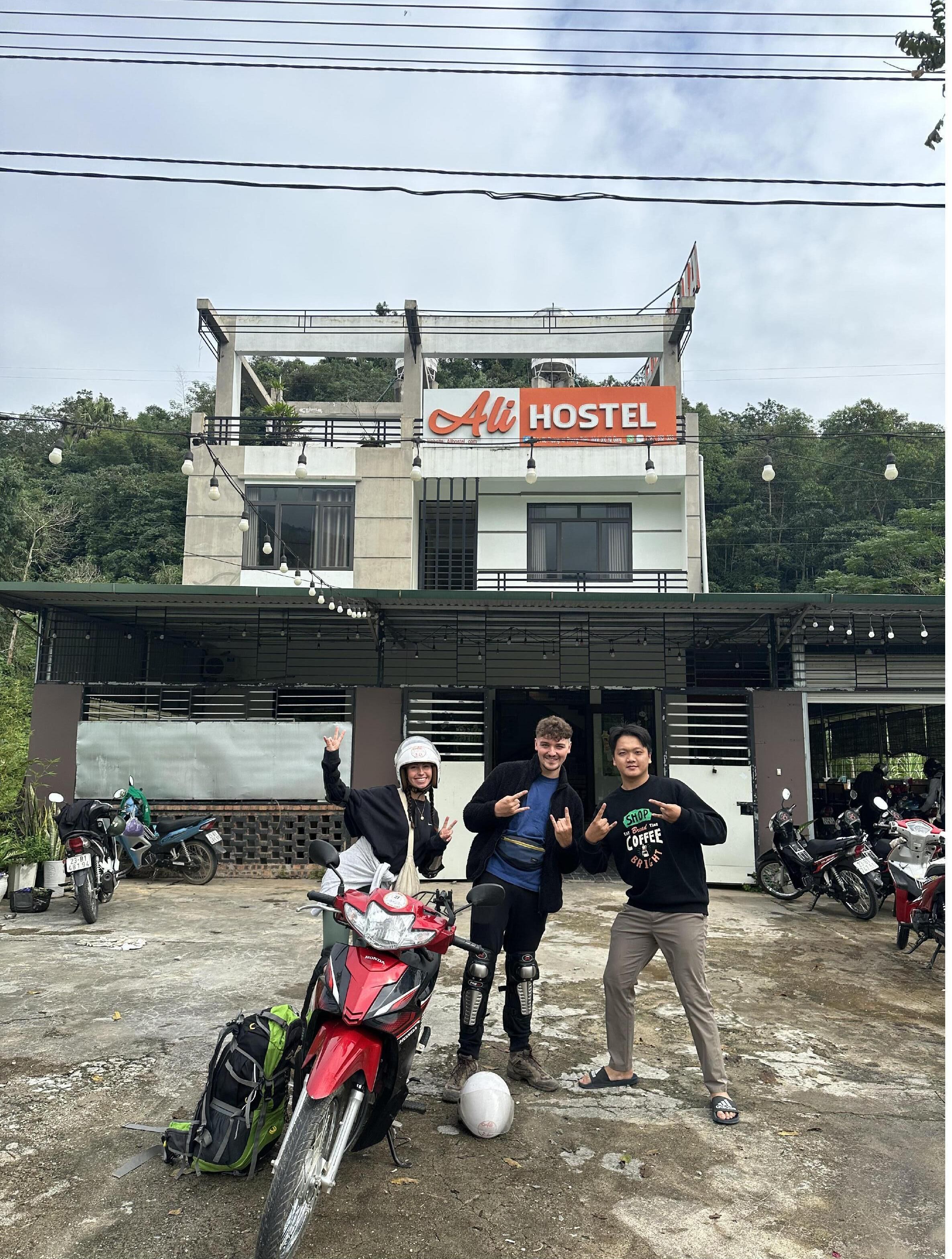 Une auberge de jeunesse avec une enseigne indiquant « ALI HOSTEL » et une moto garée devant.