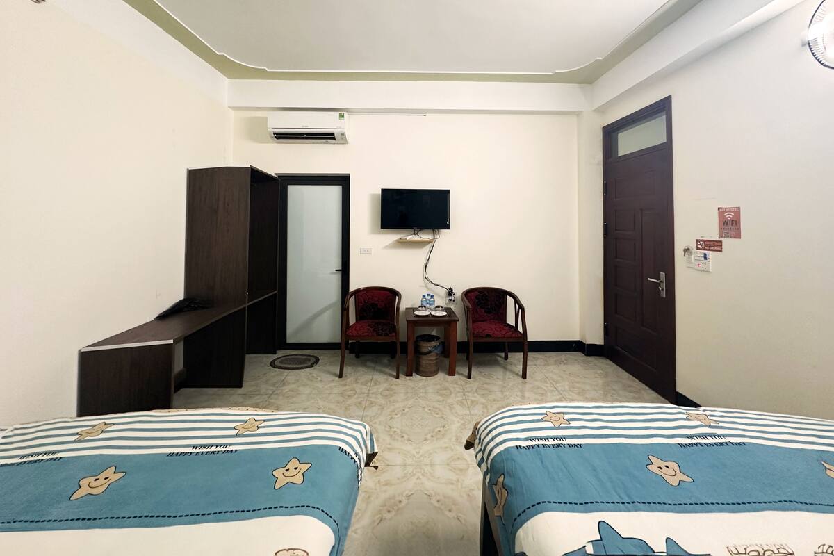 A hotel room with two beds, a TV, a desk, and a chair.