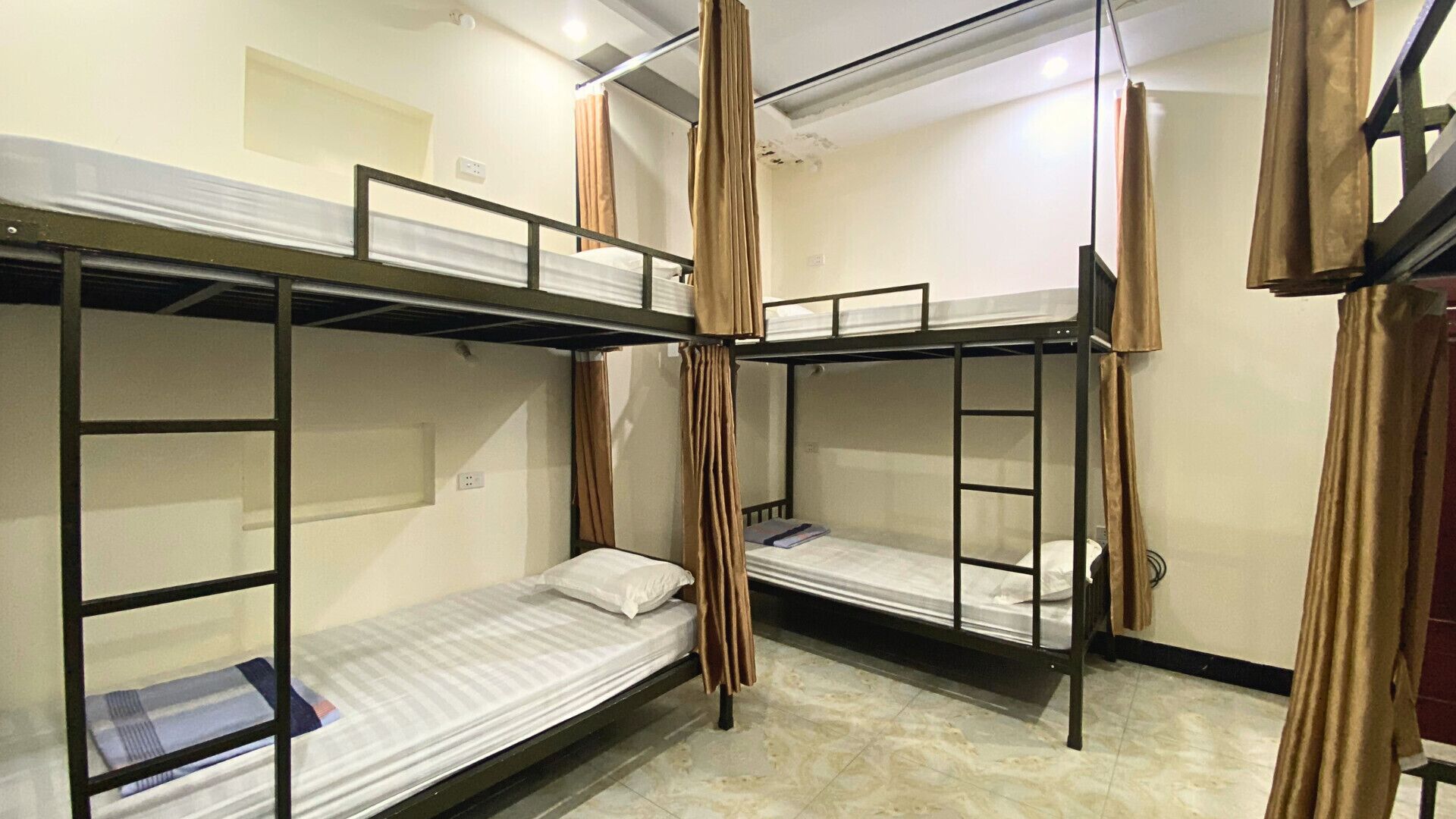 A dormitory room with bunk beds, curtains, and a tiled floor.