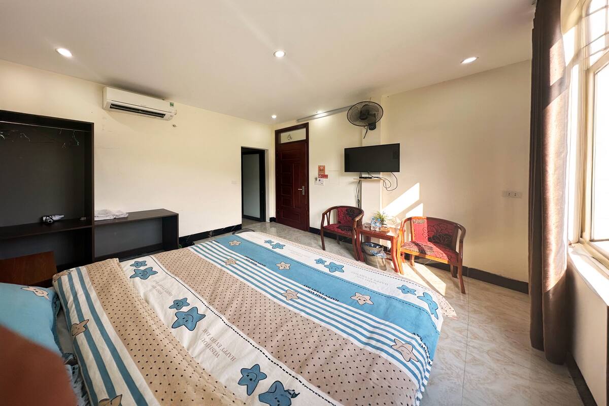 A hotel room with a bed, a TV, an air conditioner, a fan, and a window.