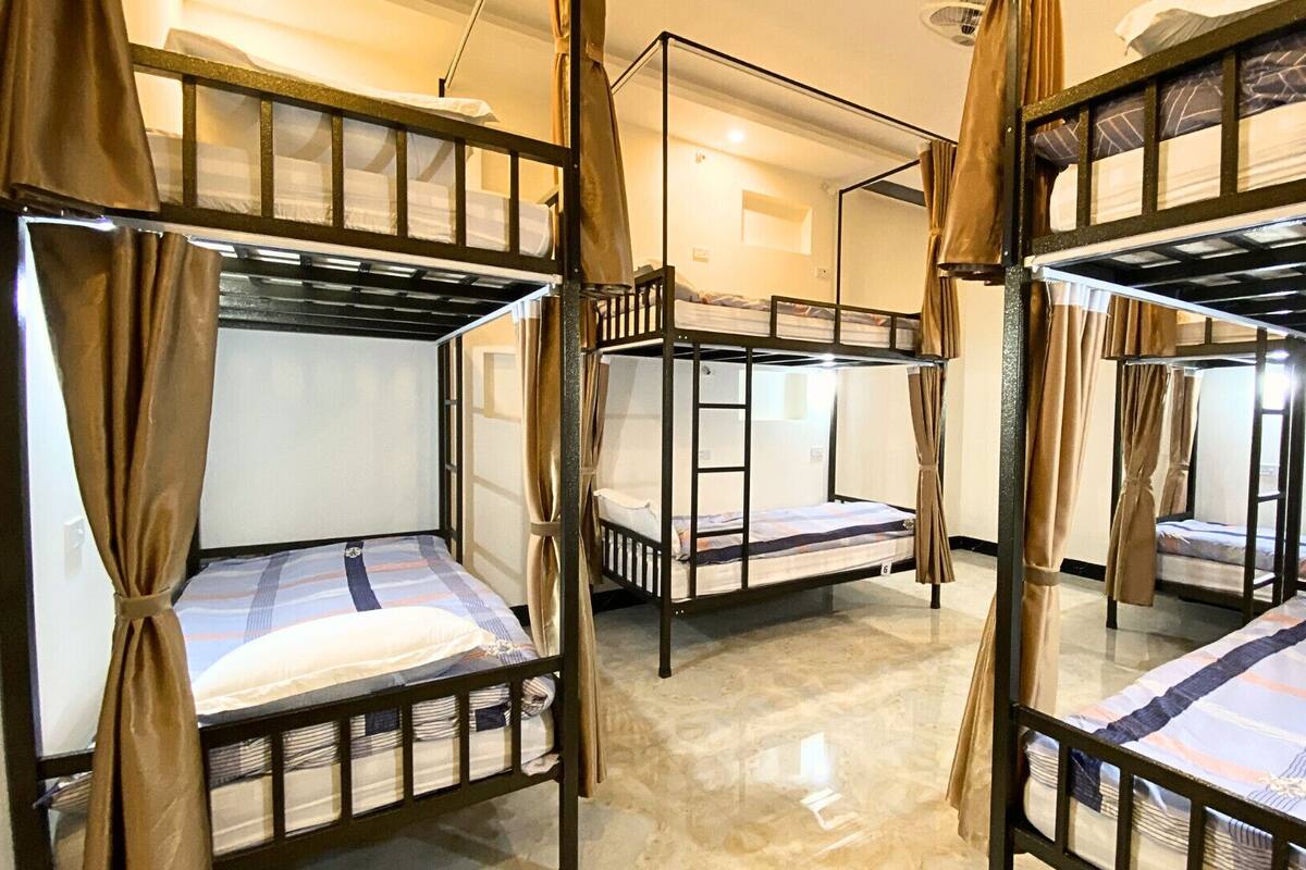 A dormitory room with bunk beds, curtains, and a ladder.