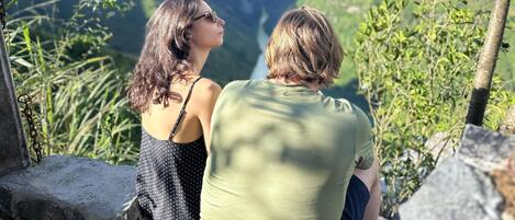 Two people sitting on a stone ledge overlooking a mountainous landscape.
