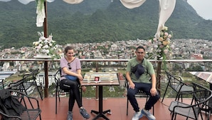 A balcony with a view of a town and mountains, featuring a table with chairs and a sign. - Ali Hostel Hà Giang (Ha Giang 1)