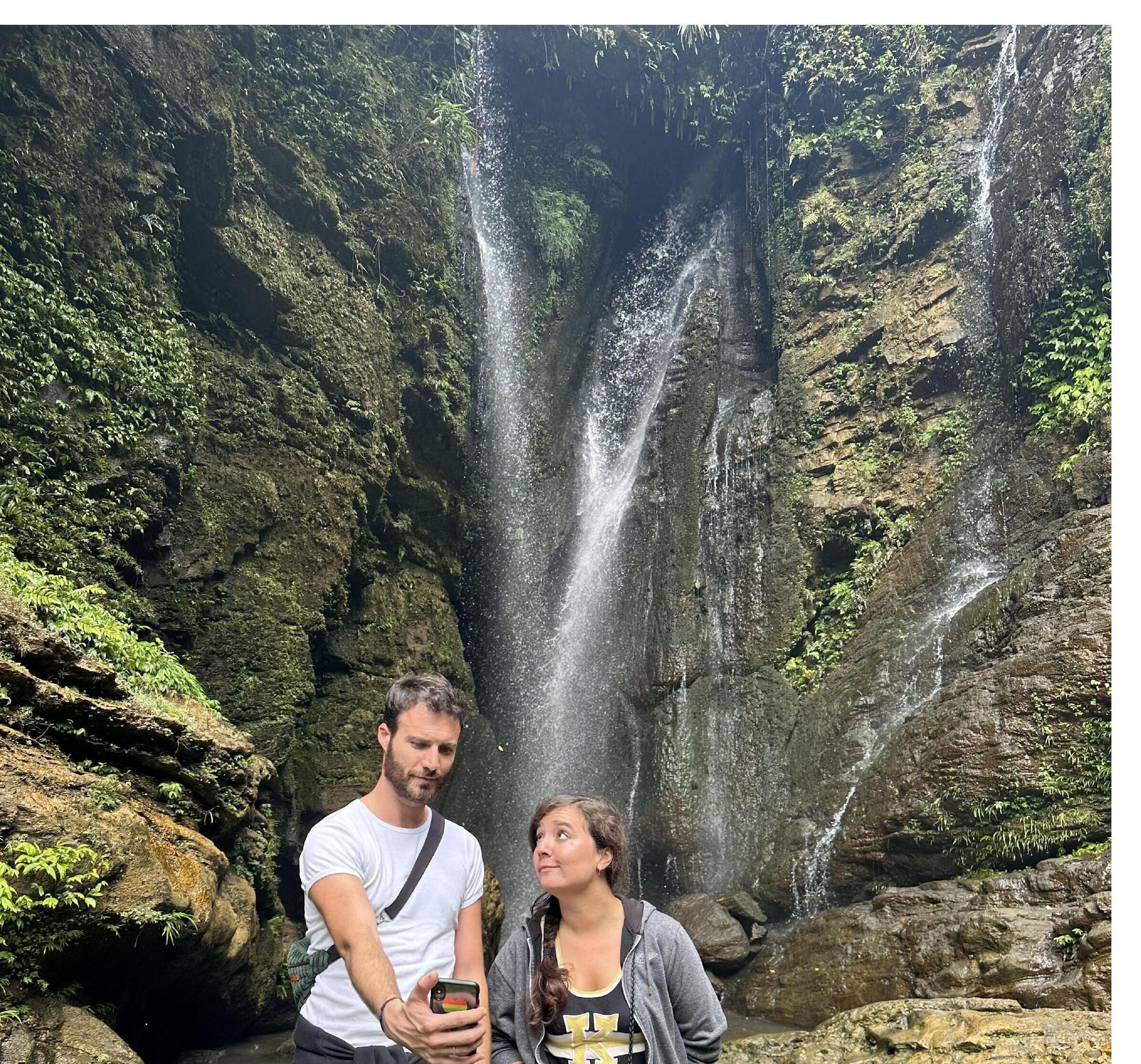 A couple standing in front of a waterfall with a rocky backdrop.