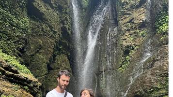 A couple standing in front of a waterfall with a rocky backdrop.