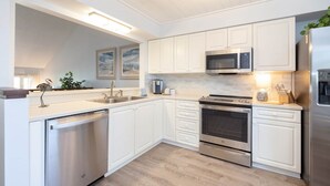Une cuisine moderne avec des meubles blancs, des appareils en acier inoxydable et un plancher en bois.