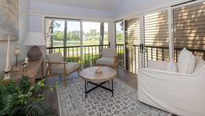 Un vaste balcon offrant une vue sur un terrain de golf, aménagé avec une table ronde, deux chaises et un canapé.