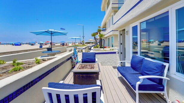 A deck with blue outdoor furniture, a fire pit, and a view of the beach. - Oceanfront Paradise - AC, Private Patio, Gas Grill, Private Washer/Dryer! (San Diego)