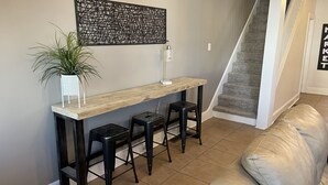 Un salon moderne avec une console en bois, des tabourets noirs, une plante en pot et un escalier.
