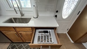 Une cuisine dotée d’un évier en acier inoxydable, de meubles en bois, d’un plan de travail blanc et d’un organiseur de tiroirs intégré avec des ustensiles.