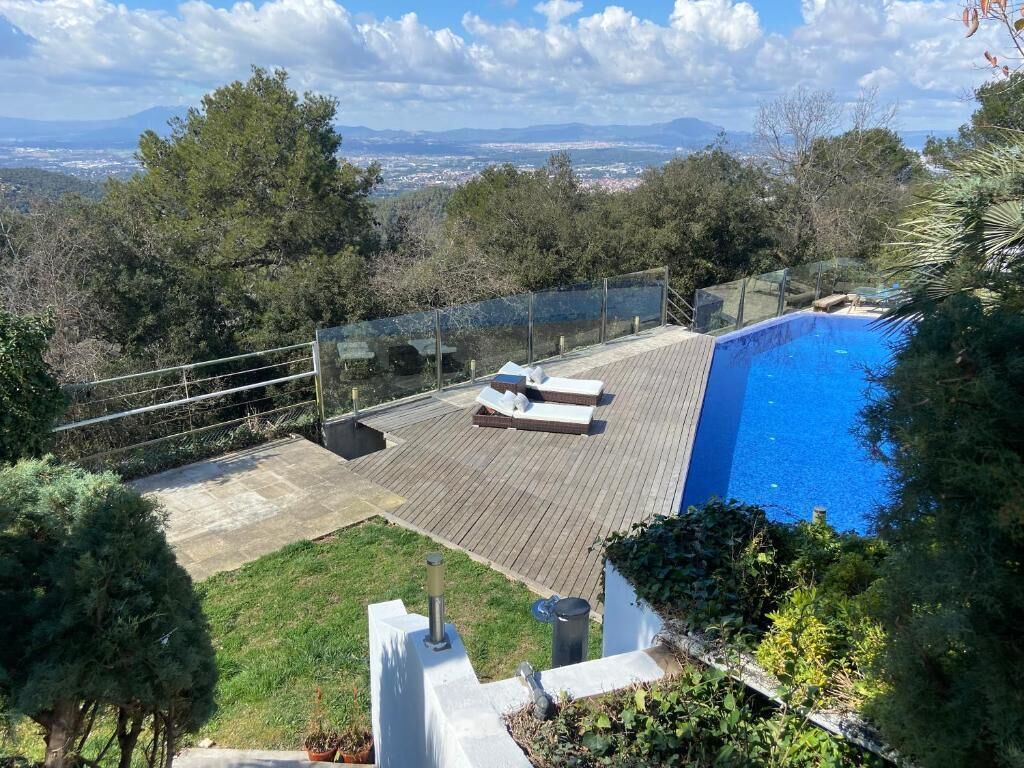 A pool with a wooden deck and lounge chairs, surrounded by greenery and trees.