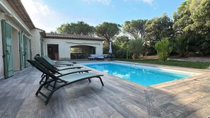 A swimming pool with lounge chairs, a covered patio, and a garden area.